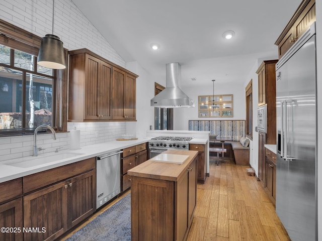 kitchen with exhaust hood, a kitchen island, built in appliances, sink, and hanging light fixtures