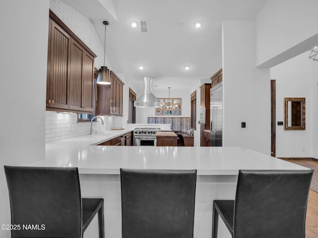 kitchen with premium appliances, island exhaust hood, kitchen peninsula, pendant lighting, and a breakfast bar area