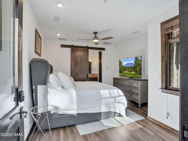 bedroom with ceiling fan, a barn door, and wood-type flooring