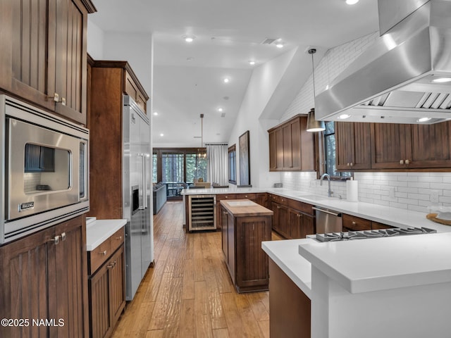 kitchen featuring built in appliances, a center island, range hood, sink, and pendant lighting