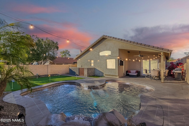 pool at dusk with area for grilling, a patio, and ceiling fan