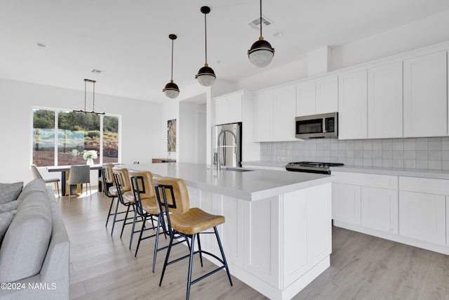 kitchen featuring hanging light fixtures, sink, white cabinets, an island with sink, and stainless steel appliances