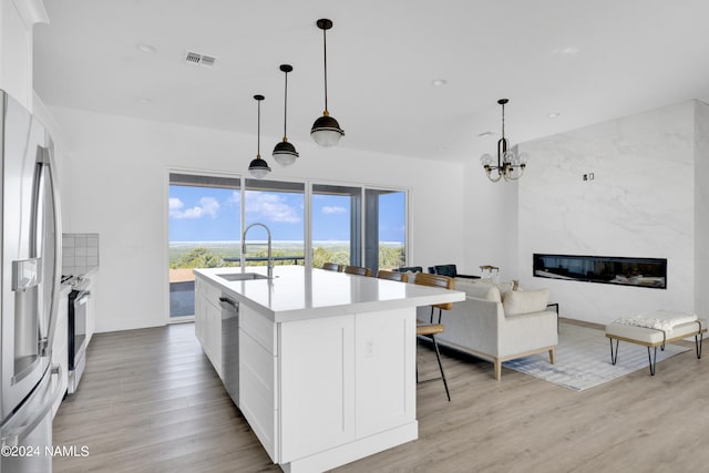 kitchen with pendant lighting, white cabinets, appliances with stainless steel finishes, sink, and a center island with sink