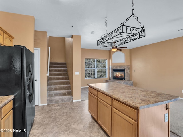 kitchen featuring light brown cabinetry, a glass covered fireplace, ceiling fan, a kitchen island, and black fridge