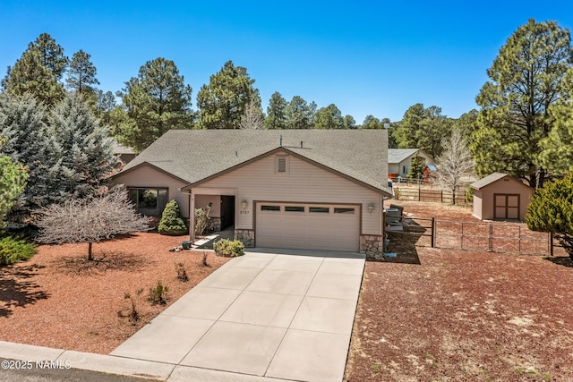 view of front of house featuring concrete driveway, stone siding, a storage shed, an attached garage, and fence