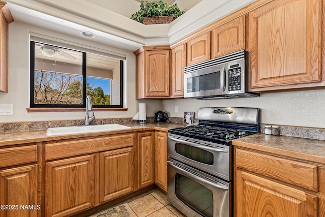 kitchen with appliances with stainless steel finishes, light tile patterned flooring, a ceiling fan, and a sink