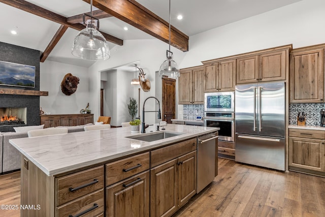 kitchen featuring sink, built in appliances, an island with sink, a fireplace, and decorative backsplash