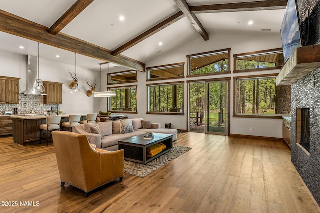 living room featuring beamed ceiling, a large fireplace, high vaulted ceiling, and light hardwood / wood-style floors