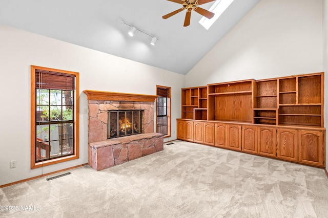3130 Tina Ln, Flagstaff, AZ 86001 - unfurnished living room featuring a stone fireplace, light colored carpet, ceiling fan, track lighting, and a skylight