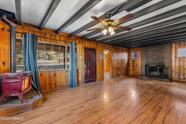 living room featuring wood-type flooring, a stone fireplace, a wood stove, ceiling fan, and beam ceiling