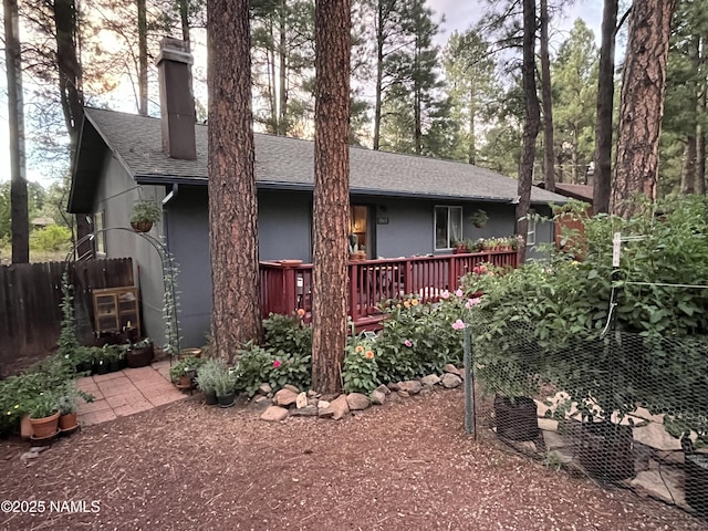 view of front of house with stucco siding, a chimney, fence, and roof with shingles