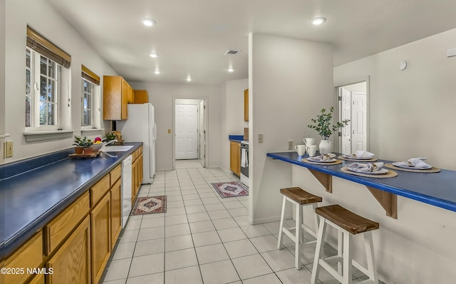8210 Winchester Dr, Flagstaff, AZ 86004 - kitchen with white appliances, dark countertops, light tile patterned floors, a breakfast bar area, and brown cabinets