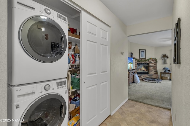 washroom featuring laundry area, stacked washer and dryer, stone finish flooring, a fireplace, and light carpet