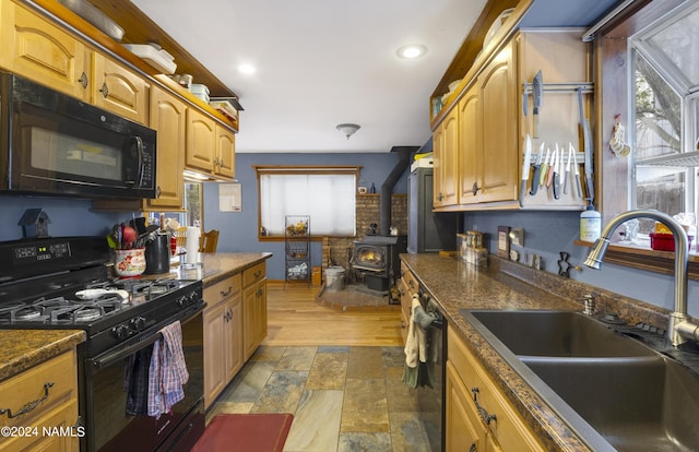 kitchen featuring sink, a wood stove, black appliances, and a wealth of natural light