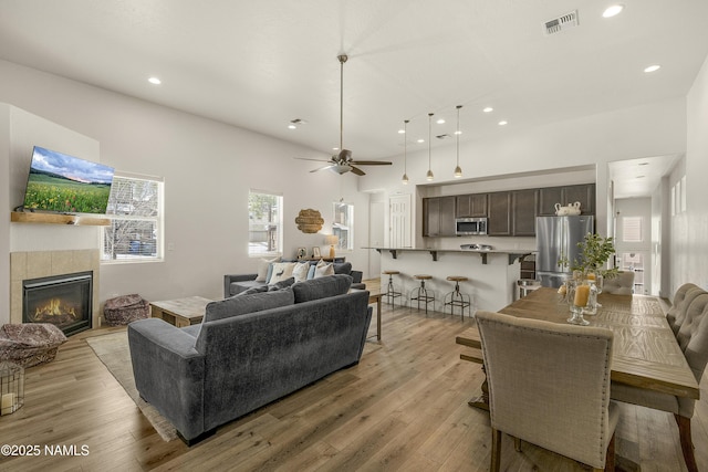 living room with light wood-style floors, recessed lighting, visible vents, and a tiled fireplace