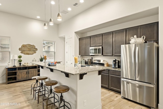 kitchen with light wood finished floors, stainless steel appliances, visible vents, dark brown cabinetry, and a kitchen breakfast bar