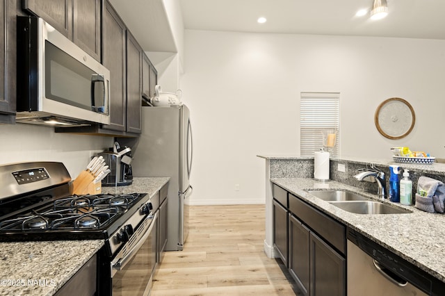 kitchen featuring light stone counters, stainless steel appliances, a sink, dark brown cabinets, and light wood-type flooring