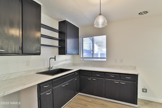 1009 Bales Ave, Winslow, AZ 86047 - kitchen featuring a sink, open shelves, light wood-style floors, dark cabinetry, and decorative light fixtures