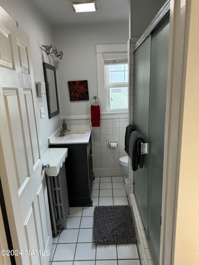 bathroom featuring toilet, a shower with shower door, tile walls, tile patterned flooring, and vanity