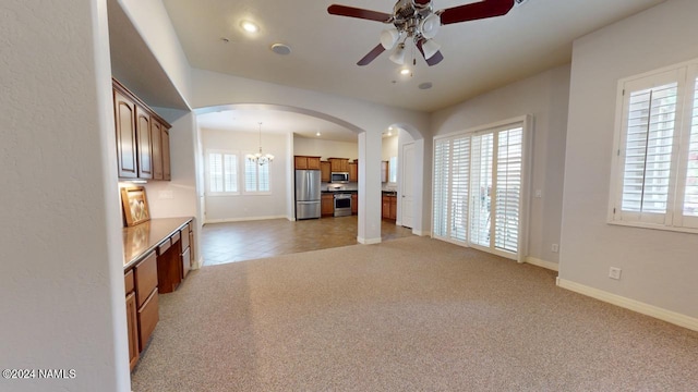 unfurnished living room with ceiling fan with notable chandelier and light colored carpet