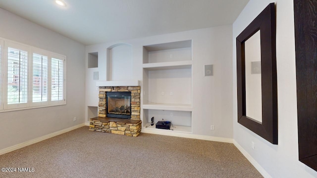 living room with built in shelves, a stone fireplace, and carpet flooring