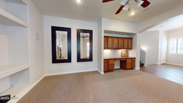 unfurnished living room featuring built in desk, ceiling fan, and light colored carpet