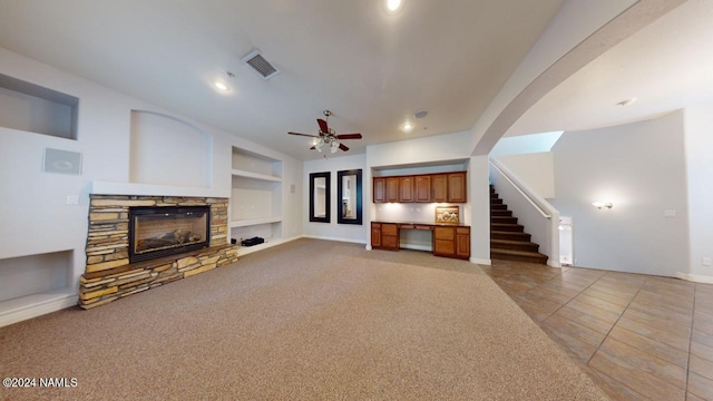 unfurnished living room with built in shelves, a stone fireplace, ceiling fan, and light tile patterned floors