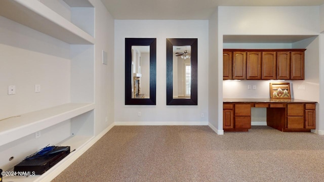 unfurnished office featuring ceiling fan, light carpet, and built in desk