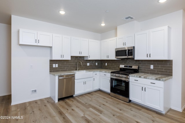 kitchen with appliances with stainless steel finishes, sink, white cabinetry, light stone counters, and light hardwood / wood-style floors