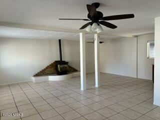 below grade area with light tile patterned floors, a wood stove, and a ceiling fan