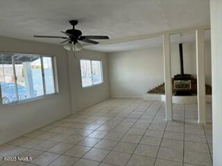 unfurnished living room featuring a wood stove, light tile patterned floors, and ceiling fan