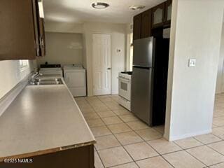 kitchen with light tile patterned floors, dark brown cabinetry, washer and dryer, white gas range oven, and freestanding refrigerator