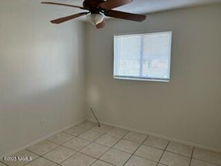 empty room featuring light tile patterned floors, a ceiling fan, and baseboards