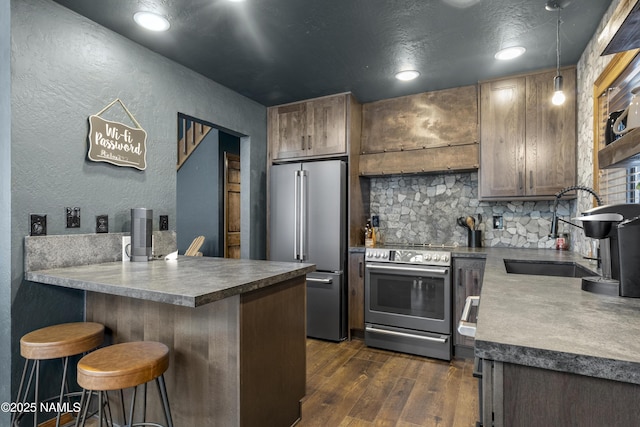 kitchen featuring dark wood-style flooring, a breakfast bar area, appliances with stainless steel finishes, a sink, and a peninsula