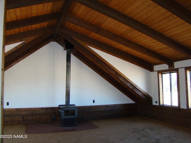 interior space with vaulted ceiling with beams, carpet floors, wooden ceiling, and a wood stove