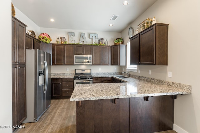 3223 S Beringer Ln, Flagstaff, AZ 86005 - kitchen with stainless steel appliances, a peninsula, dark brown cabinetry, light wood-type flooring, and a breakfast bar
