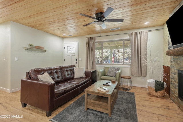 living room featuring wood ceiling, ceiling fan, a stone fireplace, and light wood-type flooring