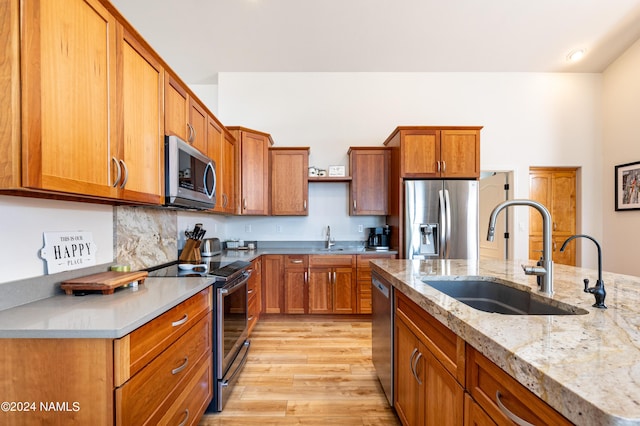 kitchen with stainless steel appliances, brown cabinetry, a sink, and light wood-style floors