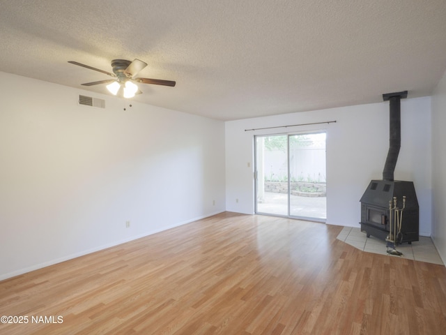 2401 N W St Unit 107, Flagstaff, AZ 86004 - unfurnished living room featuring a wood stove, a textured ceiling, light wood-style floors, ceiling fan, and baseboards