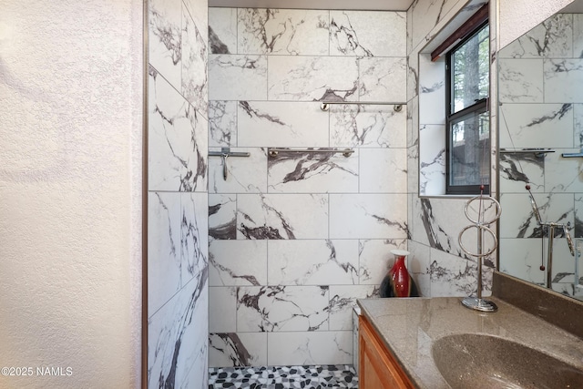 full bath with tiled shower, vanity, and a textured wall