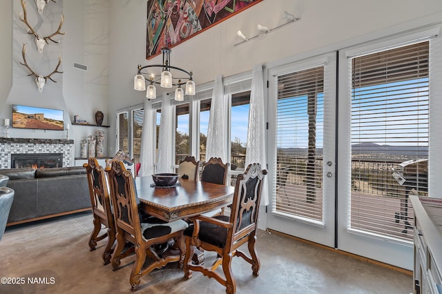 dining area with a tiled fireplace, a notable chandelier, french doors, and a high ceiling