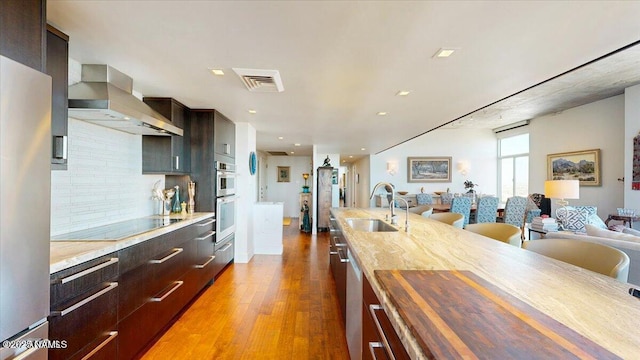 kitchen featuring visible vents, butcher block countertops, open floor plan, wall chimney exhaust hood, and appliances with stainless steel finishes