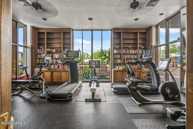 exercise room with expansive windows, a textured ceiling, ceiling fan, and visible vents