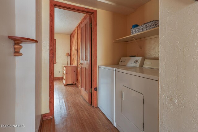 laundry area featuring light wood-type flooring, laundry area, a textured wall, and washer and clothes dryer