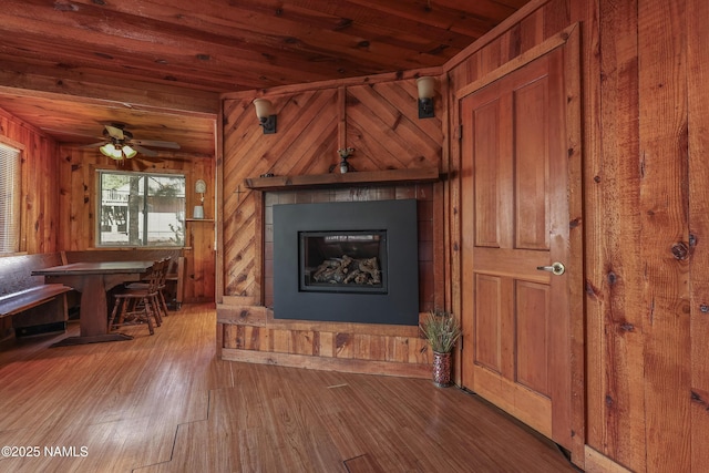 unfurnished living room with a glass covered fireplace, wooden walls, wood ceiling, and wood finished floors
