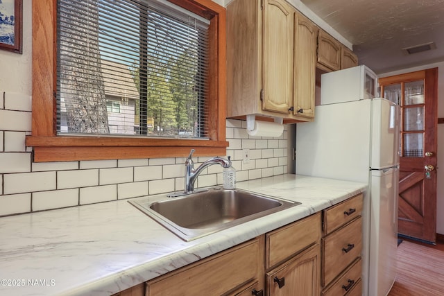 kitchen with freestanding refrigerator, tasteful backsplash, visible vents, light countertops, and a sink