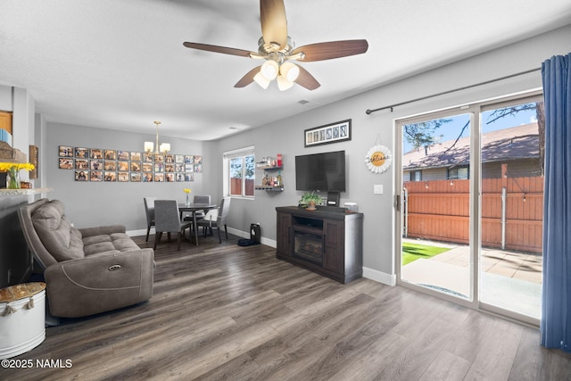 living room with ceiling fan with notable chandelier, baseboards, and wood finished floors