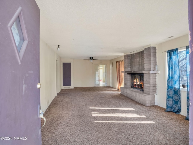unfurnished living room with ceiling fan, a brick fireplace, carpet, and a textured ceiling