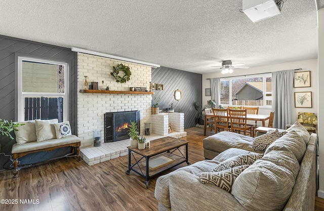 living room with a textured ceiling, a brick fireplace, wooden walls, ceiling fan, and dark hardwood / wood-style floors