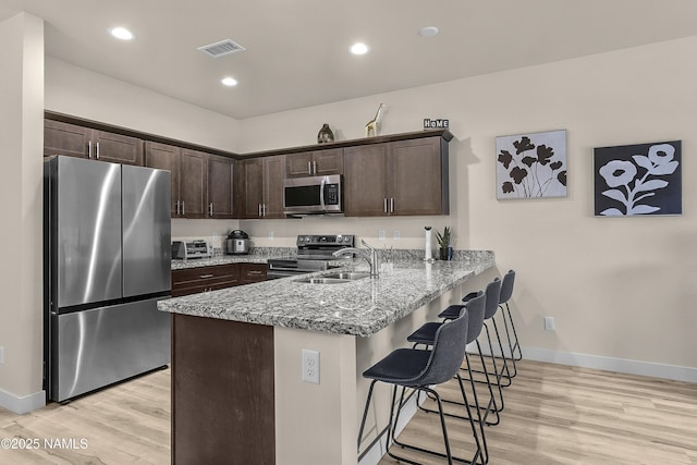kitchen featuring light wood-style flooring, a peninsula, dark brown cabinetry, and appliances with stainless steel finishes